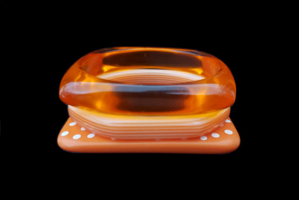 Horizontal front view of 1980s vintage orange and white square sliced polka dot, striped, and translucent solid three (3) bangle bracelet set.