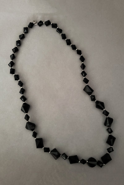 Vertical view of 1980s vintage black plastic and silver tone metal long bead necklace by Trifari.