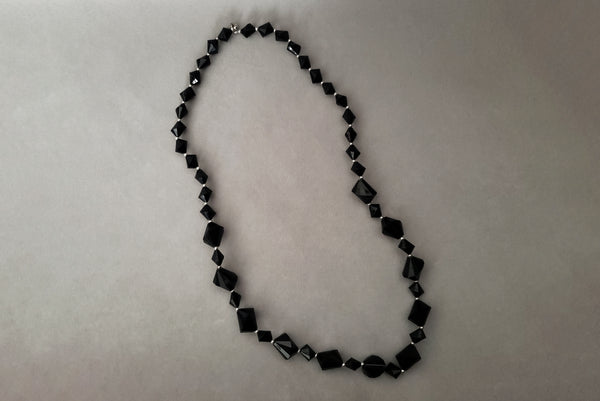 Horizontal view of 1980s vintage black plastic and silver tone metal long bead necklace by Trifari.