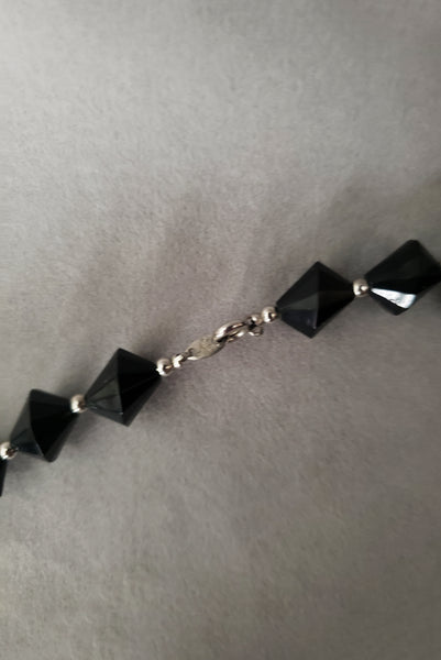 Detail view of 1980s vintage black plastic and silver tone metal long bead necklace by Trifari. Showing a close-up of the silver tone spring ring clasp.