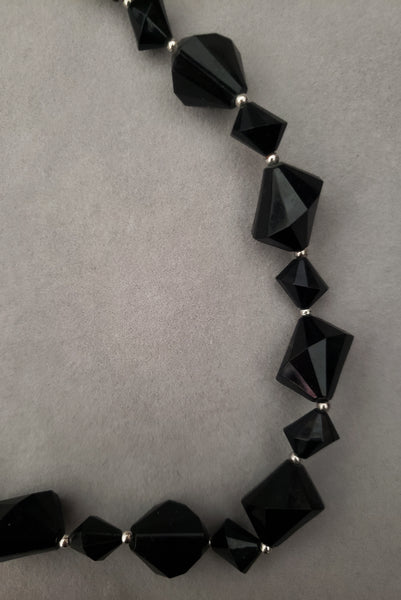 Detail view of 1980s vintage black plastic and silver tone metal long bead necklace by Trifari. Showing a close-up of the black plastic beads with small silver tone metal spacers.