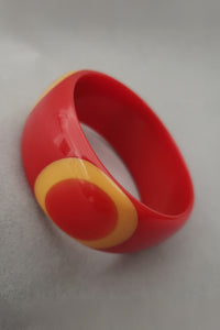 Vertical perspective view of signed Shultz tomato Bakelite bullseye bangle  bracelet with egg yolk and orange dots.