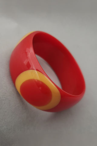 Vertical perspective view of signed Shultz tomato Bakelite bullseye bangle  bracelet with egg yolk and orange dots.