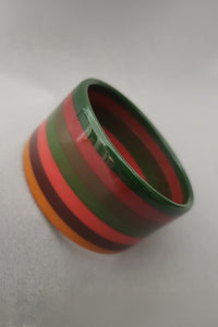 Vertical perspective view of 1990s vintage wide laminated layered striped green, red, brown, and mustard Bakelite bangle bracelet. Possibly a MOE piece.