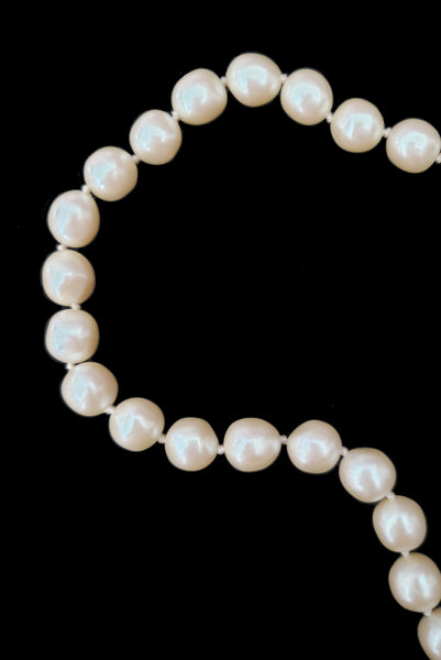 Detail view of 1980s vintage cream faux pearl long beaded necklace. Shown on a display. Showing a close-up of the beads on string with knots in between.