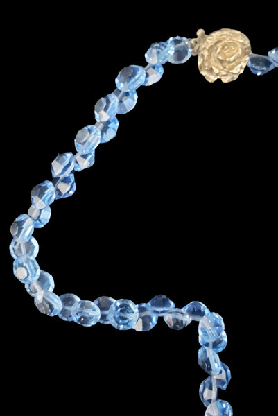 Detail view of 1980s vintage blue faceted round crystal long beaded necklace with silver tone rose clasp. Showing a close-up of the faceted round, flat, blue beads and silver tone rose shaped slide clasp.
