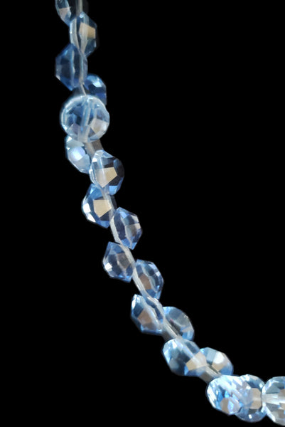 Detail view of 1980s vintage blue faceted round crystal long beaded necklace with silver tone rose clasp. Showing a close-up of the faceted round, flat, blue beads.
