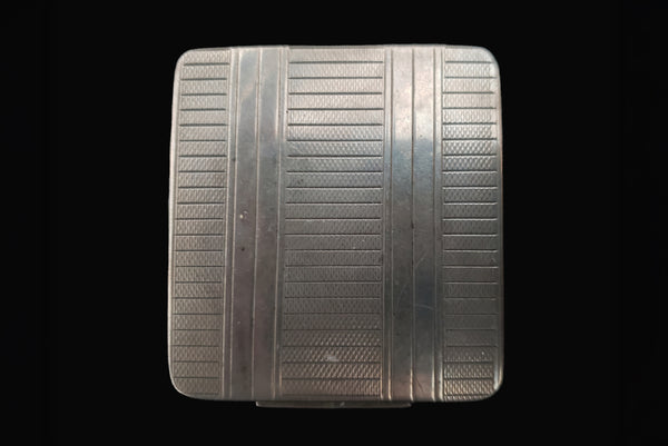 Horizontal top view of 1920s vintage square silver tone stripe engraved make-up compact.