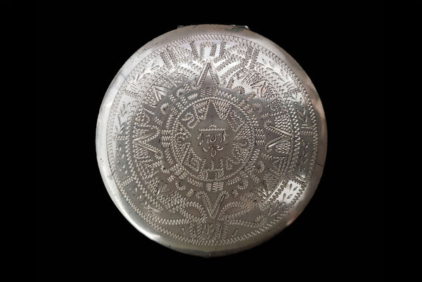Horizontal top view of 1950s vintage round sterling silver Aztec calendar engraved make-up compact.