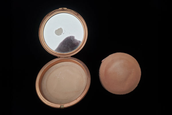 Horizontal open view of 1930s vintage Art Deco black and white enamel round gold metal mesh make-up compact by Elgin. Showing the powder puff removed and the vintage powder covered by a fabric screen.