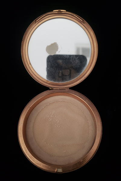 Vertical open view of 1930s vintage Art Deco black and white enamel round gold metal mesh make-up compact by Elgin. Showing the powder puff removed and the vintage powder covered by a fabric screen.