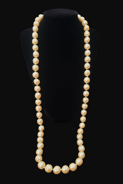 Vertical view of 1980s vintage cream faux pearl long beaded necklace. Shown on a display.