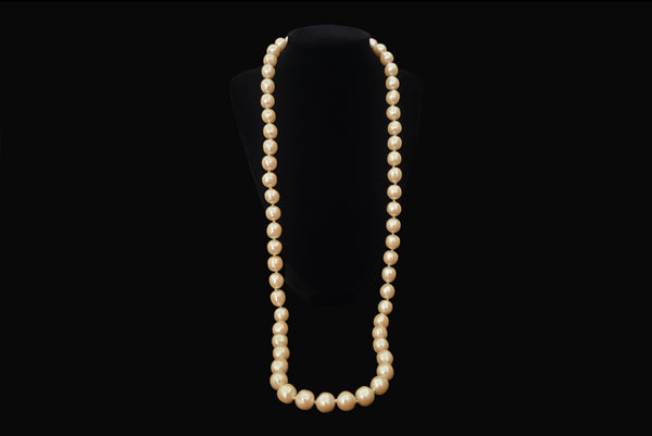 Horizontal view of 1980s vintage cream faux pearl long beaded necklace. Shown on a display.