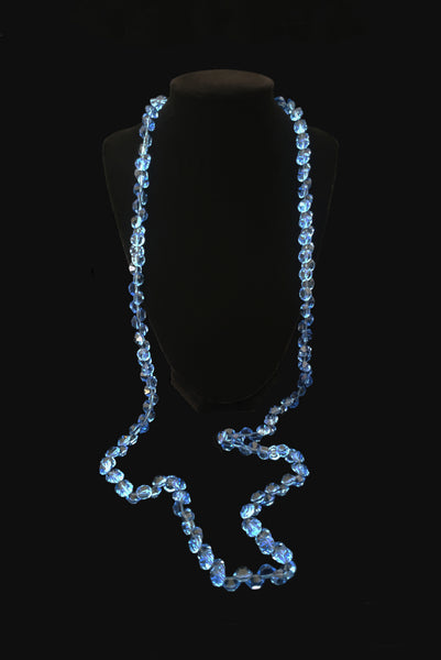 Vertical front view of 1980s vintage blue faceted round crystal long beaded necklace with silver tone rose clasp. Showing the necklace on a display stand.