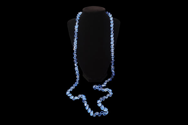 Horizontal front view of 1980s vintage blue faceted round crystal long beaded necklace with silver tone rose clasp. Showing the necklace on a display stand.