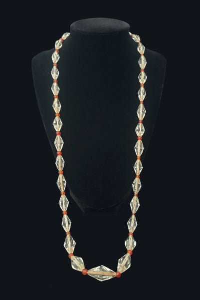 Vertical view of 1920s vintage graduated bicone clear crystal bead necklace with orange amber colored round glass spacers. Showing the necklace on a display.