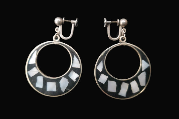 Horizontal side view of 1950s vintage alpaca silver and white abalone shell inlaid in black drop hoop screw back earrings.