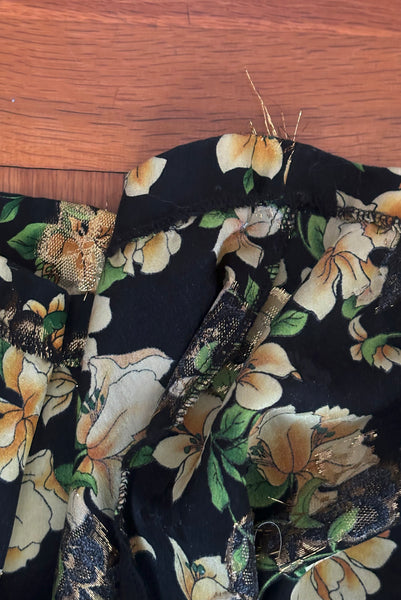 Detail view of vintage 2000s made 1940s reproduction black, yellow, and gold floral silk and lurex evening dress, size medium to large. Showing some pulled lurex threads at the hem.