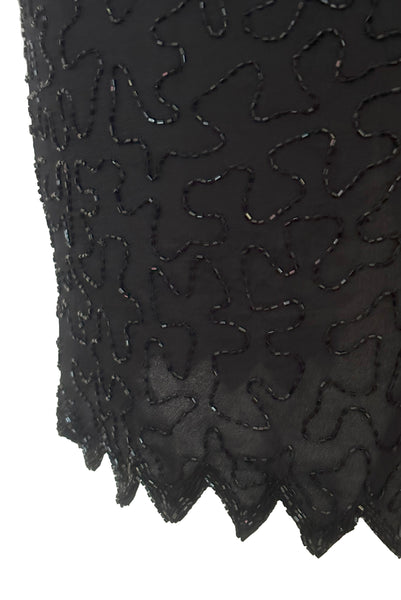 Detail view of 1980s vintage diamonds black beaded and sequin silk chiffon crew neck, short sleeve, fitted knee length cocktail dress by Laurence Kazar, size medium to large. Showing a close-up of the glass beading, and the sawtooth hem on the skirt.