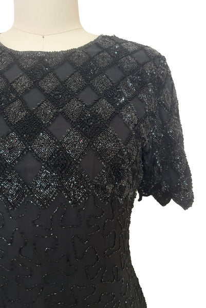 Detail view of 1980s vintage diamonds black beaded and sequin silk chiffon crew neck, short sleeve, fitted knee length cocktail dress by Laurence Kazar, size medium to large. Showing a close-up of the sequin diamond pattern on the bust & shoulders, and the sawtooth hem on the sleeves.