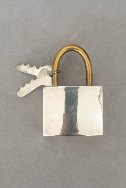 Vertical front view of 1960s vintage Mexican 925 sterling silver and brass hollow padlock and key two tone statement brooch.