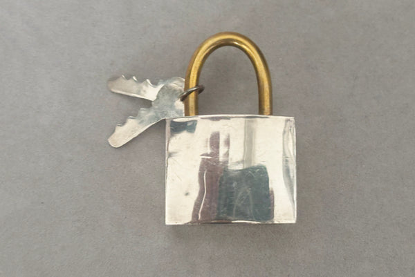 Horizontal front view of 1960s vintage Mexican 925 sterling silver and brass hollow padlock and key two tone statement brooch.