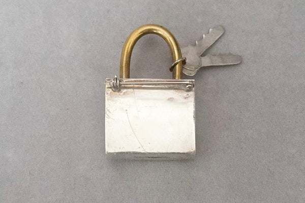 Horizontal front view of 1960s vintage Mexican 925 sterling silver and brass hollow padlock and key two tone statement brooch.