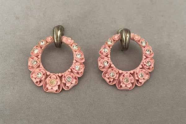 Horizontal front view of 30s vintage pink floral carved celluloid and rhinestone silver tone screw back hoop earrings.