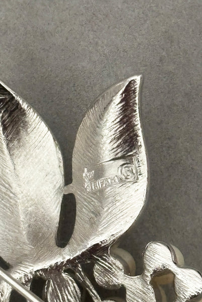 Detail view of 1960s vintage Crown Trifari white pearl silver tone grape cluster brooch and clip-on earrings jewelry set. Showing the Crown Trifari stamp on the brooch.
