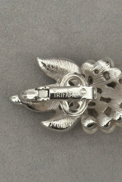 Detail view of 1960s vintage Crown Trifari white pearl silver tone grape cluster brooch and clip-on earrings jewelry set. Showing the Crown Trifari stamp on the earrings.