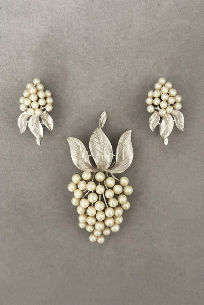 Vertical front view of 1960s vintage Crown Trifari white pearl silver tone grape cluster brooch and clip-on earrings jewelry set.