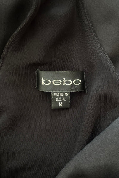 Interior detail view of 1990s vintage black silk Lycra charmeuse and rayon jersey drop waist halter dress with handkerchief hem by Bebe, size small to medium. Showing the Bebe label and size M tag.
