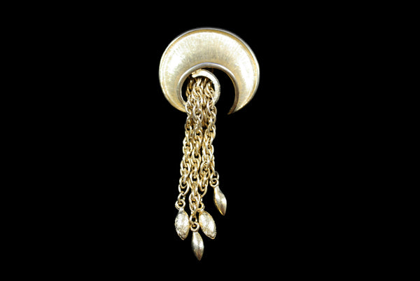 Horizontal front view of 1960s vintage round swirl gold tone brooch with chain tassel.