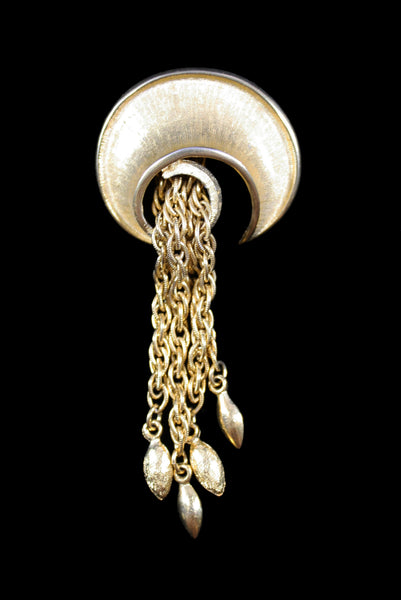 Vertical front view of 1960s vintage round swirl gold tone brooch with chain tassel.