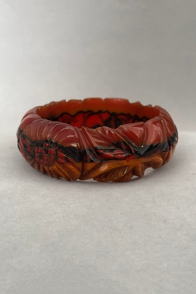 Vertical side view of 1940s vintage butterscotch, black, and red  floral carved end of day Bakelite bangle bracelet. Inscribed: "to the one I love".