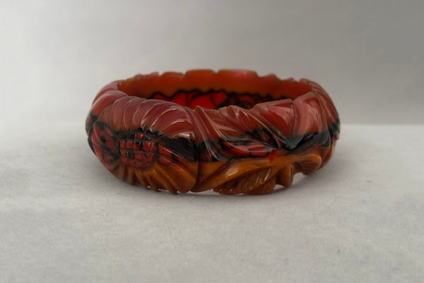 Horizontal side view of 1940s vintage butterscotch, black, and red  floral carved end of day Bakelite bangle bracelet. Inscribed: "to the one I love".