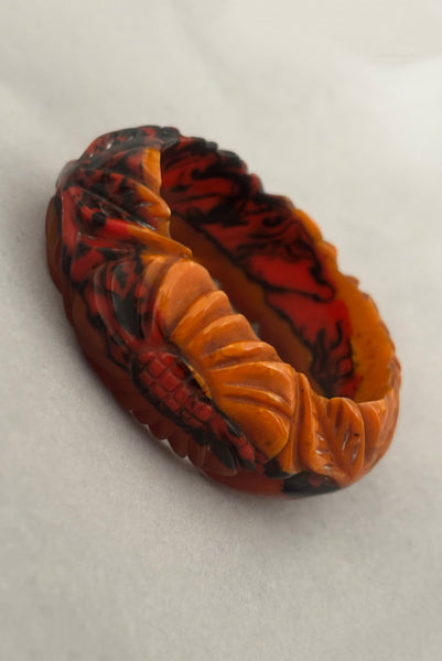 Vertical perspective view of 1940s vintage butterscotch, black, and red  floral carved end of day Bakelite bangle bracelet. Inscribed: "to the one I love".