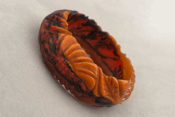 Horizontal perspective view of 1940s vintage butterscotch, black, and red  floral carved end of day Bakelite bangle bracelet. Inscribed: "to the one I love".