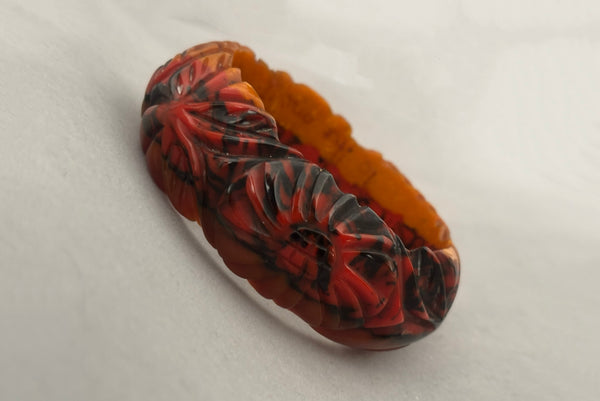 Horizontal perspective view of 1940s vintage butterscotch, black, and red  floral carved end of day Bakelite bangle bracelet. Inscribed: "to the one I love".
