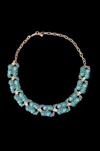 Vertical front view of 1950s vintage teal blue textured plastic bead and iridescent rhinestone silver tone necklace.