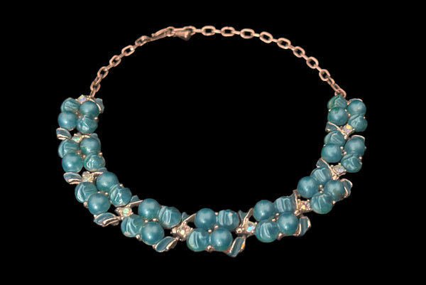 Horizontal perspective view of 1950s vintage teal blue textured plastic bead and iridescent rhinestone silver tone necklace.