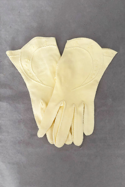 Vertical pair view of 1950s vintage pastel yellow cotton wrist length curved cuff embroidered gloves. Approximately size 7.5.