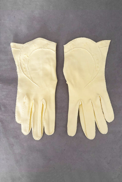 Vertical front view of 1950s vintage pastel yellow cotton wrist length curved cuff embroidered gloves. Approximately size 7.5.