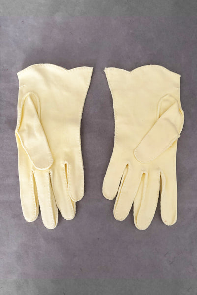 Vertical back view of 1950s vintage pastel yellow cotton wrist length curved cuff embroidered gloves. Approximately size 7.5.