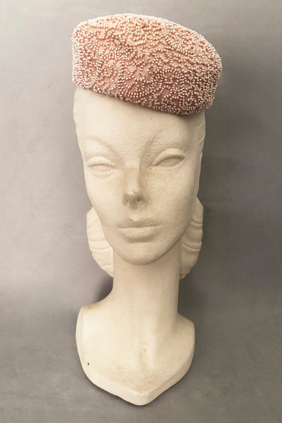 Vertical front view of 1960s vintage blush pink faille fabric pillbox hat covered in matching glass seed beads by Neiman Marcus.