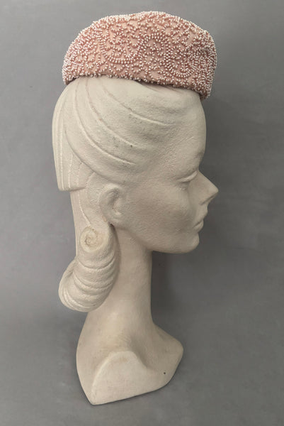 Vertical side view of 1960s vintage blush pink faille fabric pillbox hat covered in matching glass seed beads by Neiman Marcus.