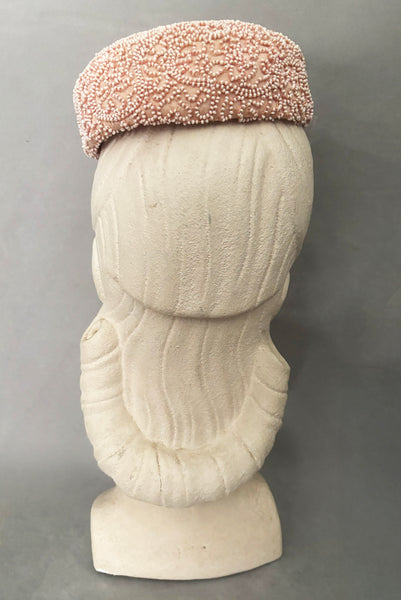 Vertical back view of 1960s vintage blush pink faille fabric pillbox hat covered in matching glass seed beads by Neiman Marcus.