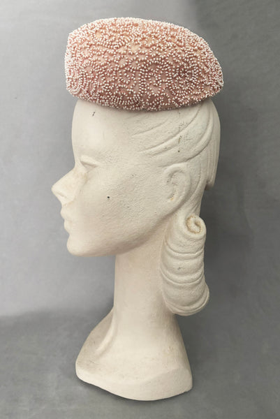 Vertical side view of 1960s vintage blush pink faille fabric pillbox hat covered in matching glass seed beads by Neiman Marcus.