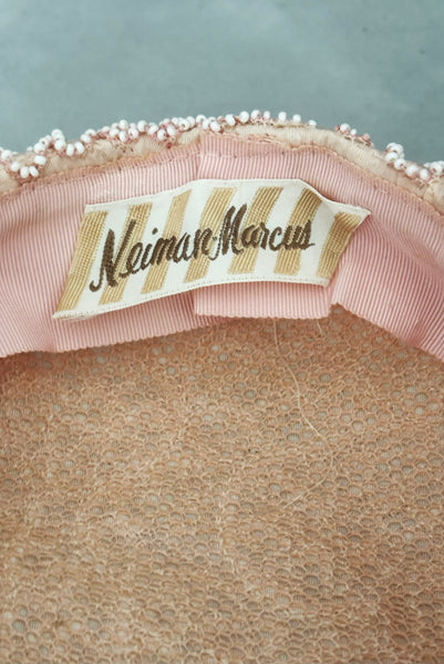 Detail view of 1960s vintage blush pink faille fabric pillbox hat covered in matching glass seed beads by Neiman Marcus. Showing a close-up of the Neiman Marcus label.