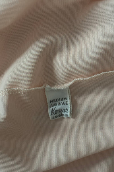 Interior detail view of 1950s vintage pale pastel pink nylon half slip with mesh and lace hem by Komar Lingerie, size small to medium. Showing the Komar Lingerie medium average label.